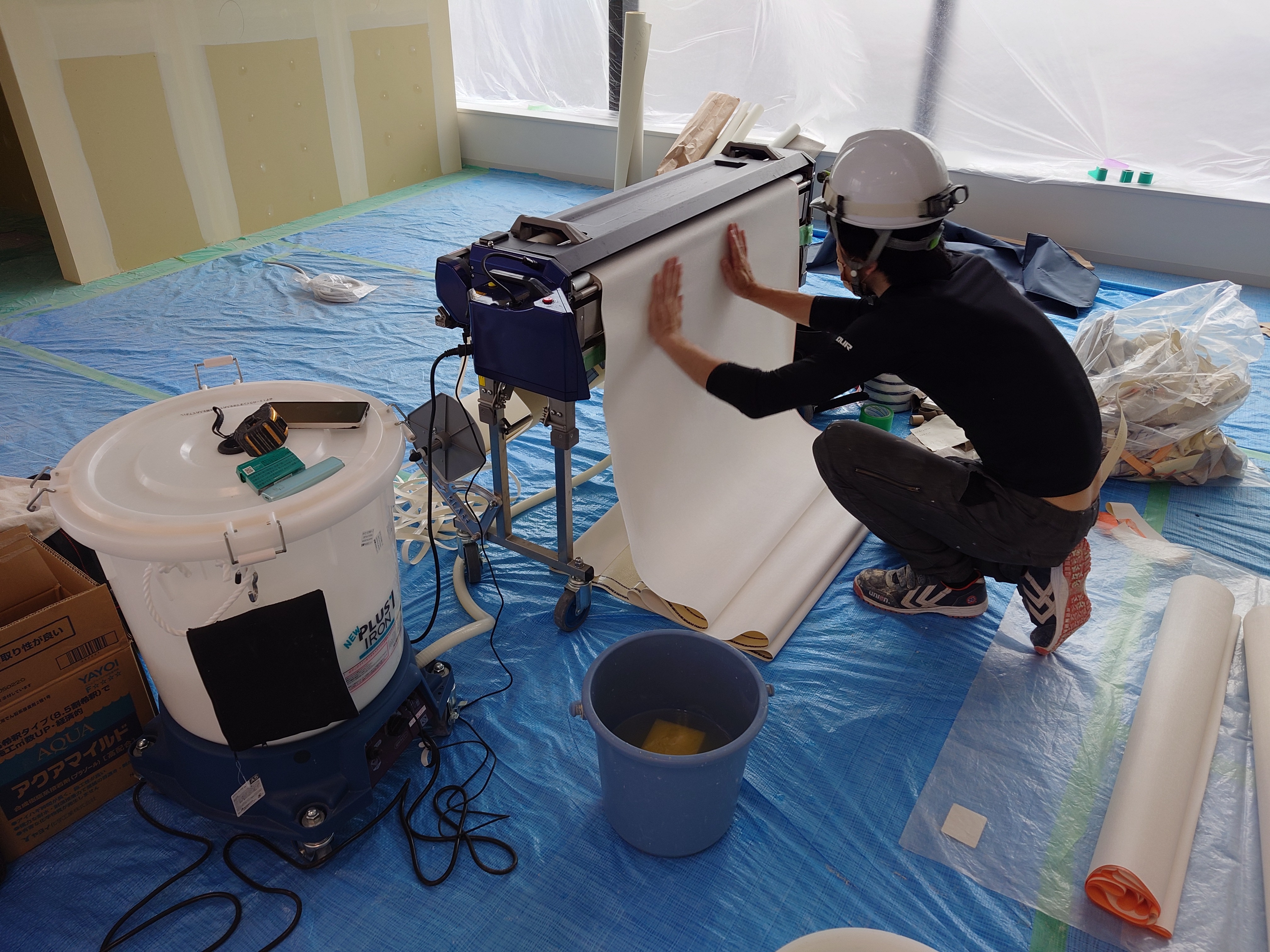 床を養生した施工区画でクロス糊付け機を準備する作業員